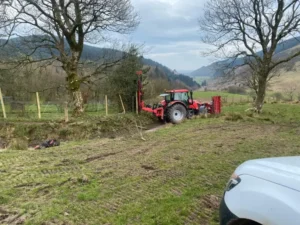 Adam Jackson Fencing red tractor laying wooden posts along a field